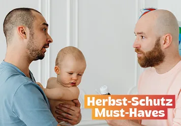 Herbst-Schutz Must-Haves: Vater mit Baby auf dem Arm. Ein anderer Mann reicht Medizin: Hausapotheke.